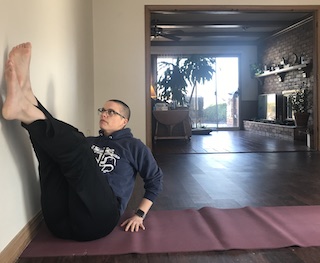 person sitting on floor with right hip against wall rasing legs up, rotating to touch feet on wall