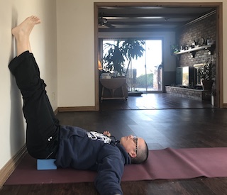 person lying on floor with legs resting against wall with yoga block under head