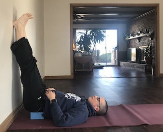 person lying on floor with legs resting against wall with yoga block under low back