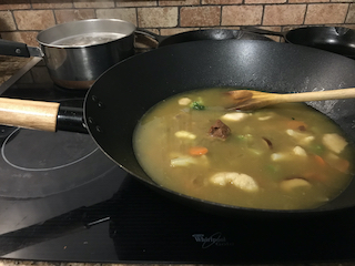 wok containing aromatics, frozen veggies, miso paste, and veggie stock cooking on the stove