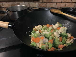 wok containing aromatics and frozen veggies cooking on the stove