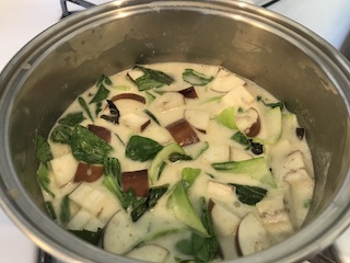 A pot on a stove filled with coconut-based Thai curry, eggplant, and basil leaves